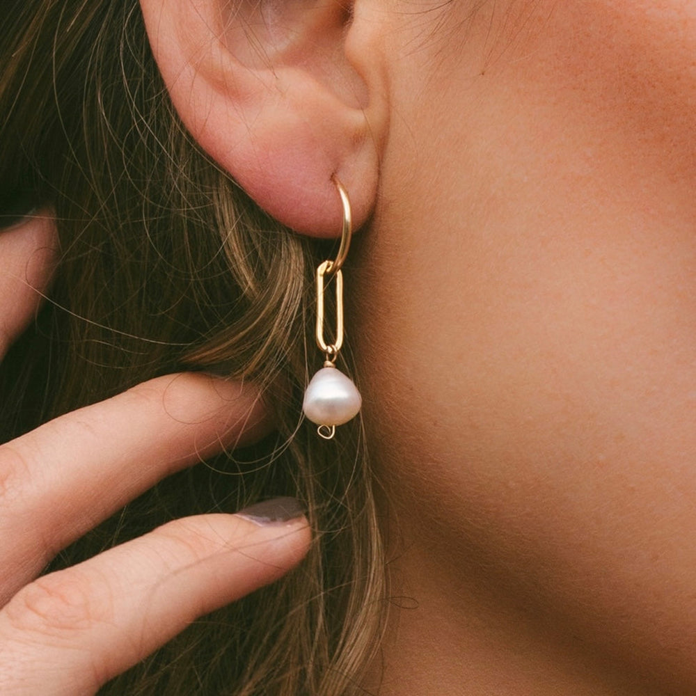Gold hoop earring with a pearl drop worn by a person