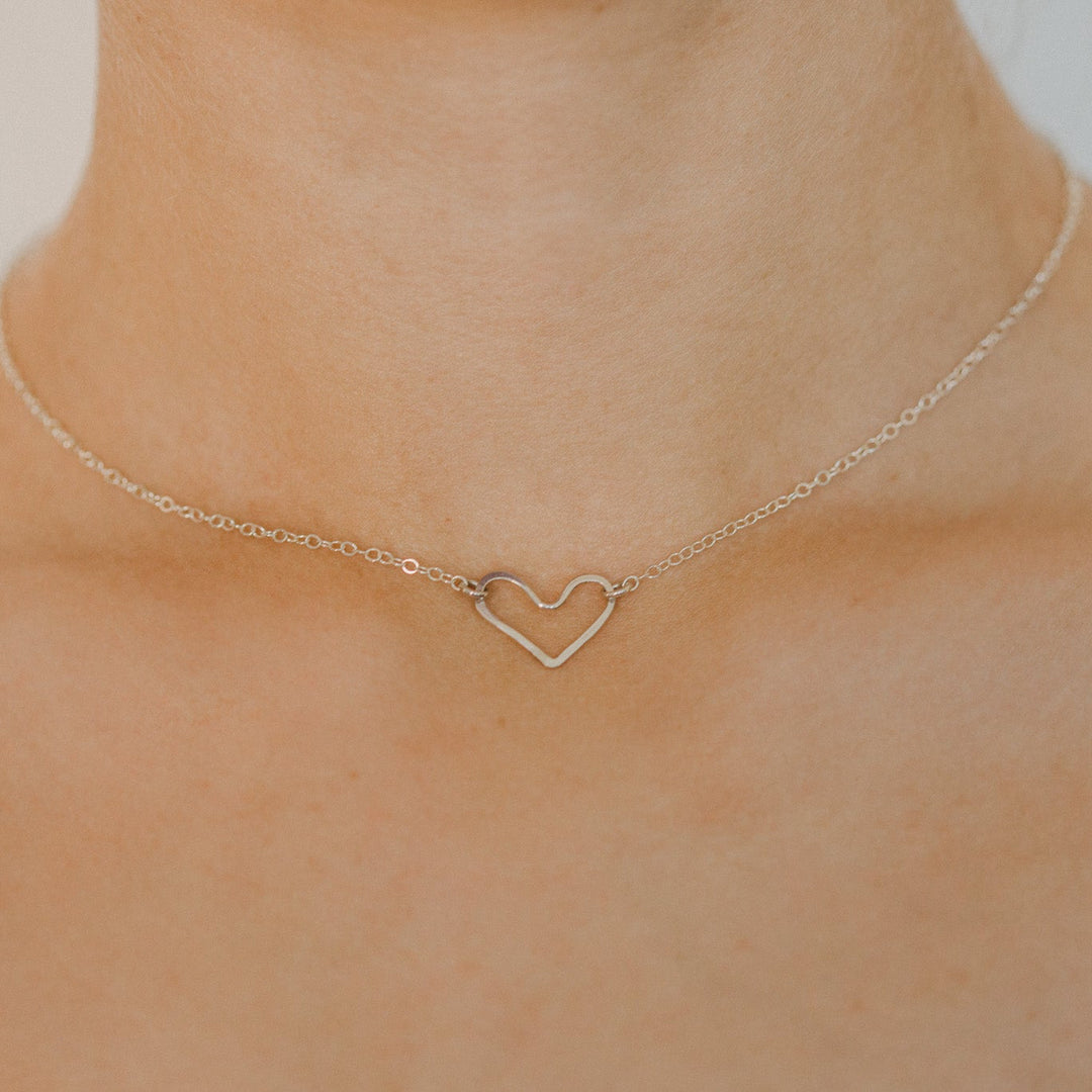 Gold necklace with a heart pendant on a person's neck against a neutral background