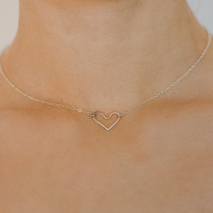 Gold necklace with a heart pendant on a person's neck against a neutral background