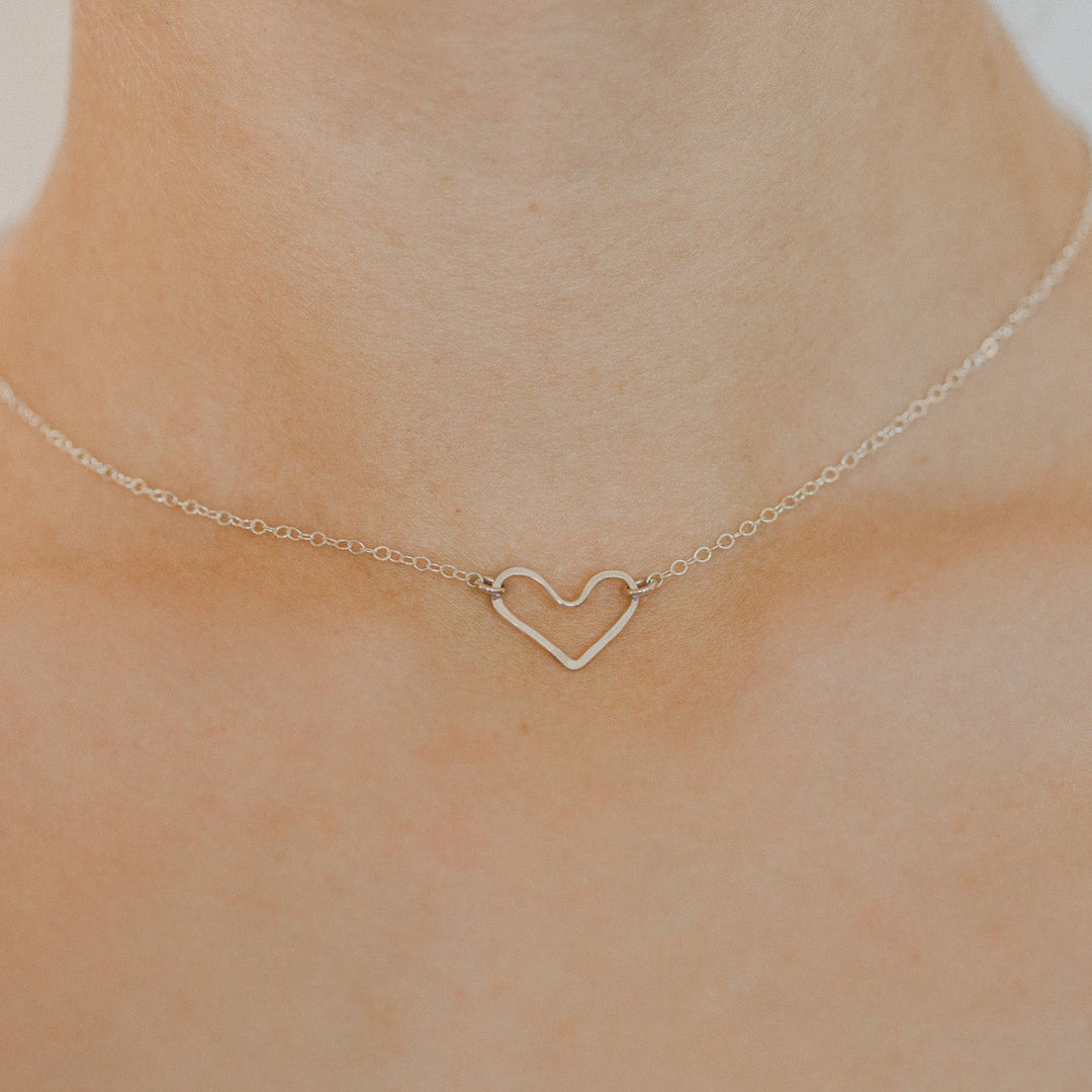 Gold heart-shaped necklace on a person's neck against a neutral background