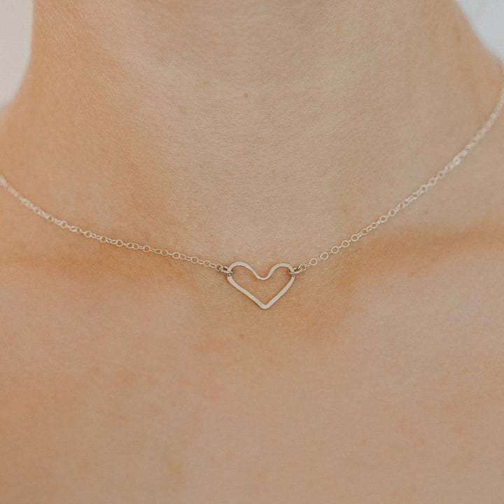 Gold heart-shaped necklace on a person's neck against a neutral background