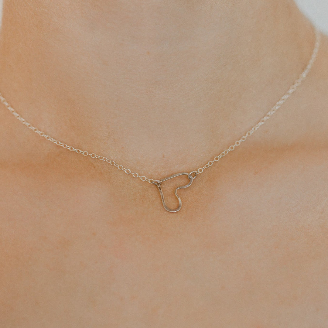 Gold heart-shaped necklace on a person's neck against a neutral background