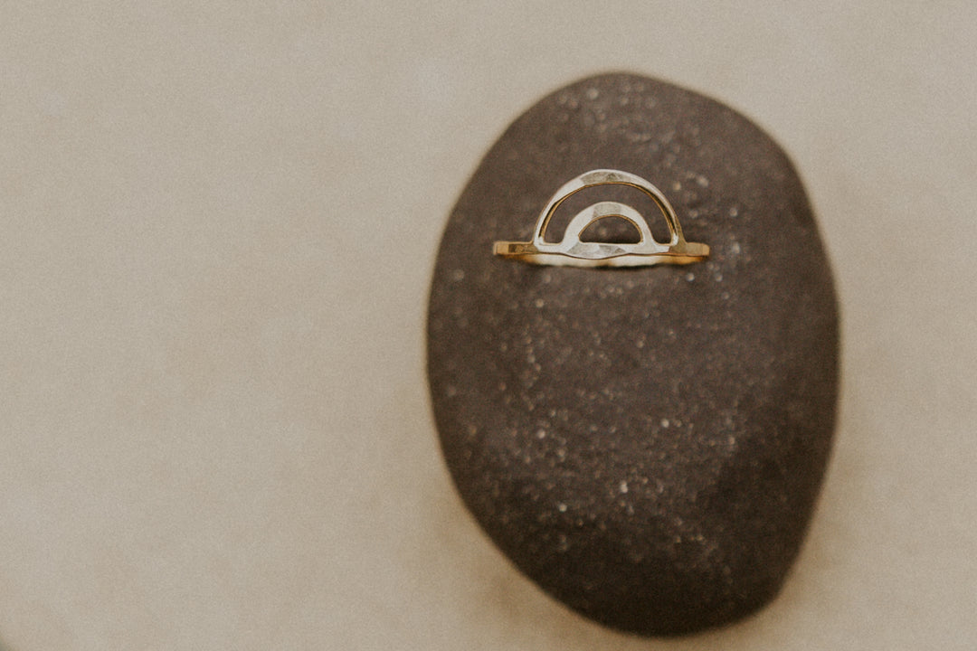 gold rainbow aloha ring on a rock with blurred background