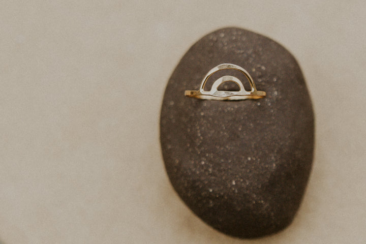 gold rainbow aloha ring on a rock with blurred background