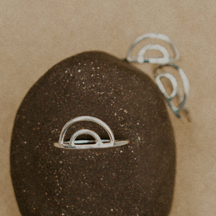 3 silver rainbow shaped rings resting on a rock