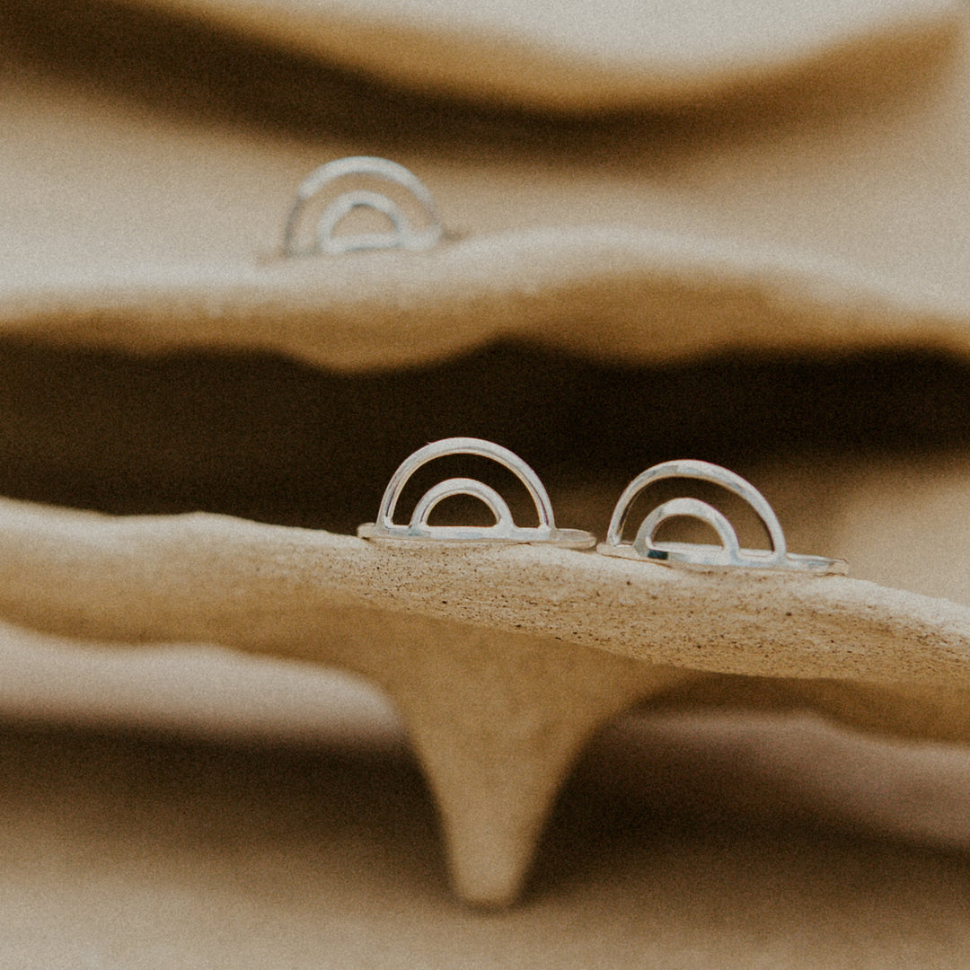 silver rainbow shaped rings resting on a  beige pottery