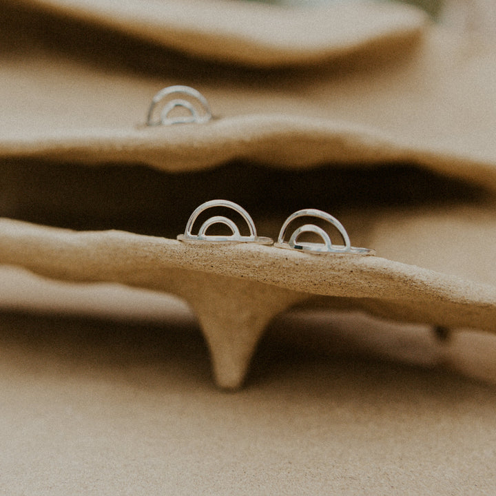 Silver rainbow-shaped rings on a beige handmade pottery