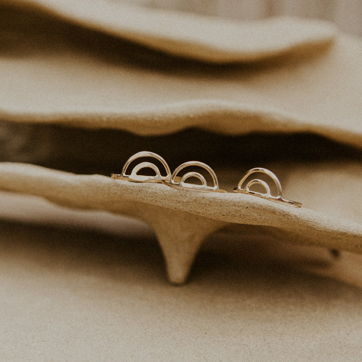 3 gold rainbow shaped rings on beige pottery handmade