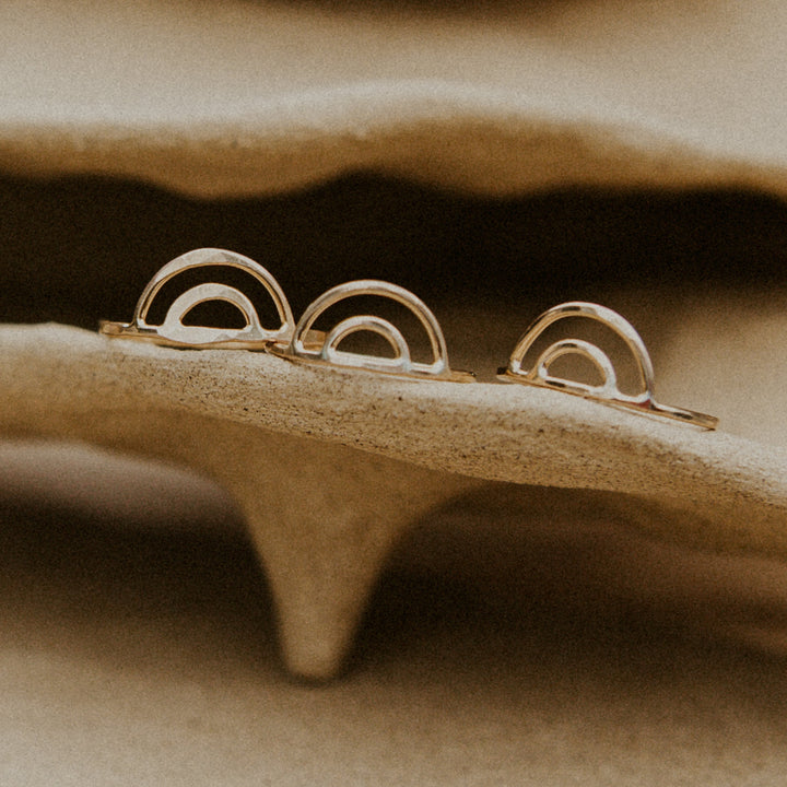 3 gold rainbow shaped rings on beige handmade pottery