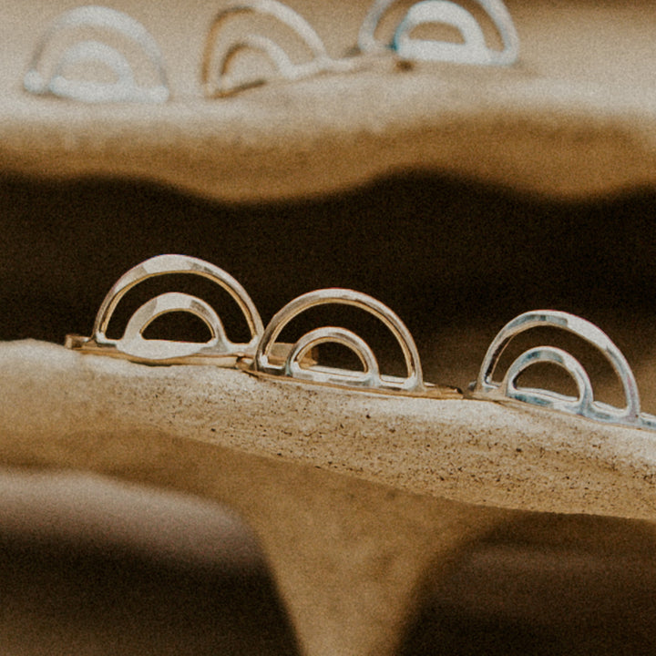 gold and silver rainbow shaped rings stacked on handmade beige clay pottery