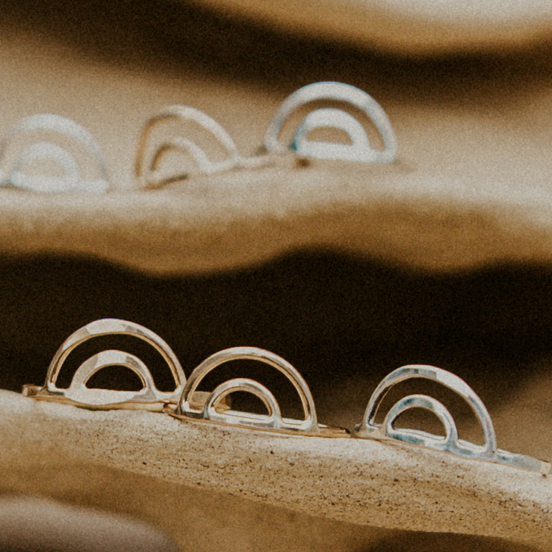 gold and silver rainbow shaped rings on handmade beige clay pottery