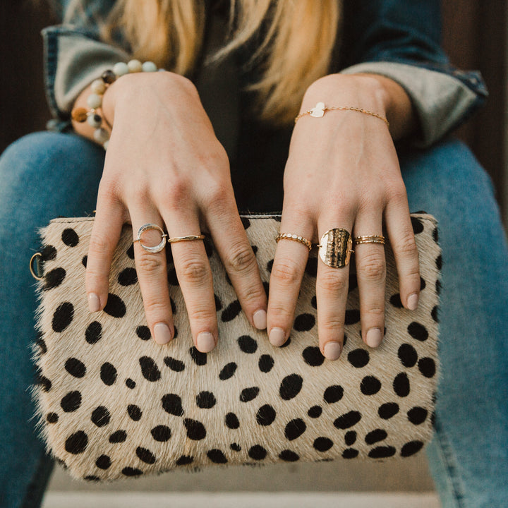 Person holding a polka dot clutch with multiple rings on fingers