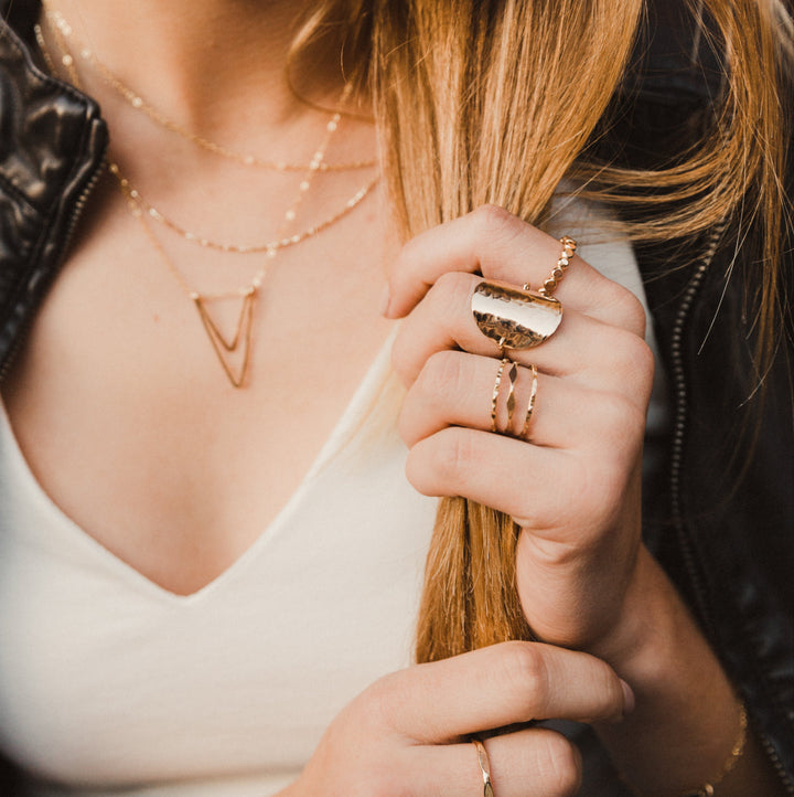 Close-up of a person holding hair with gold stacked rings and disc ring on hand

