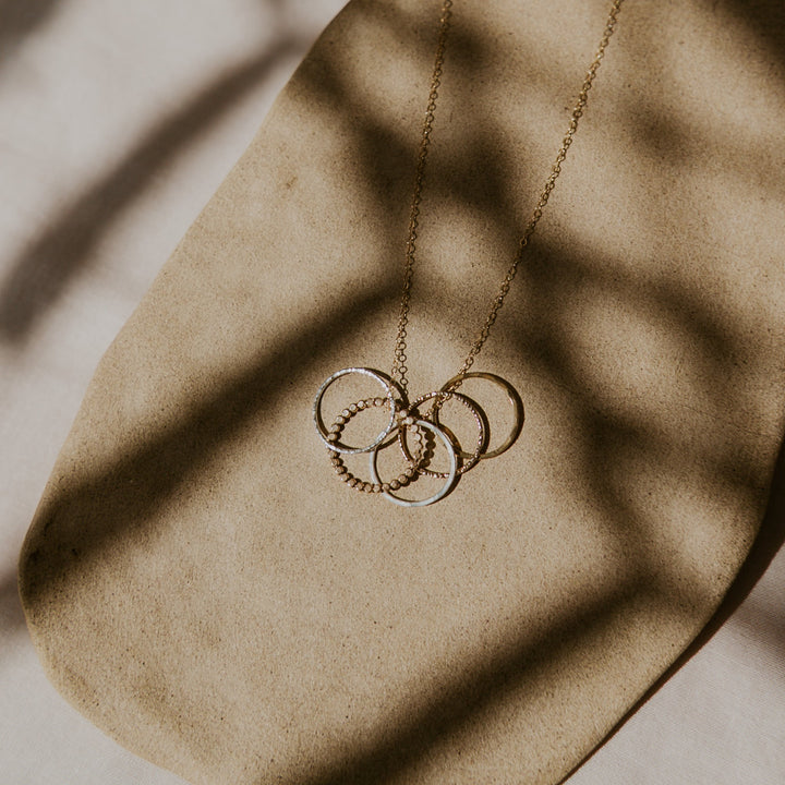 Gold necklace with interlocking rings on a textured beige surface
