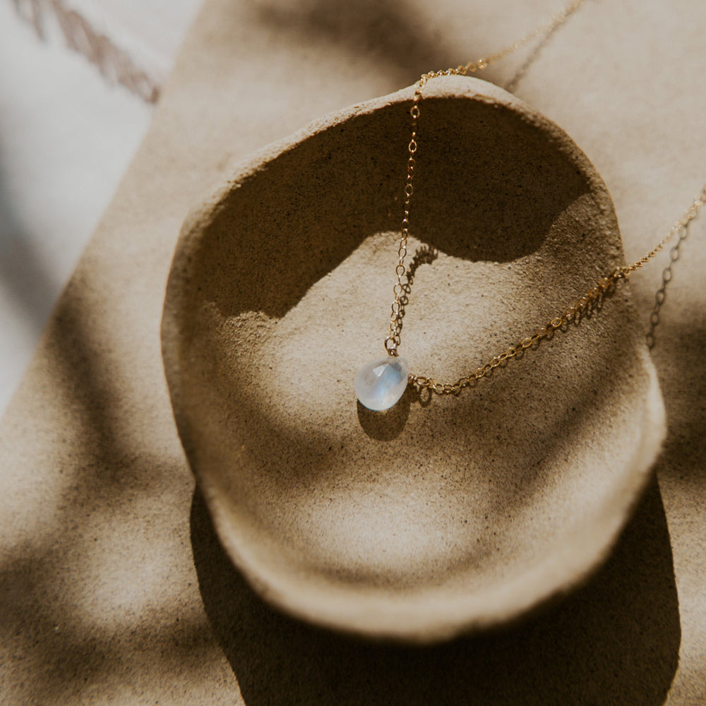 Delicate gold necklace with a pendant on a textured beige surface