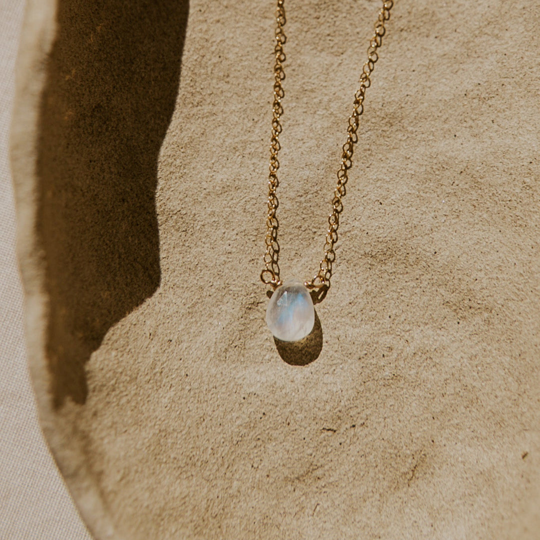Gold necklace with a moonstone pendant on a textured beige surface