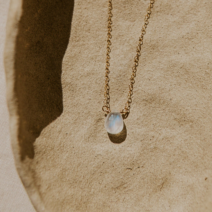 Gold necklace with a moonstone pendant on a textured beige surface