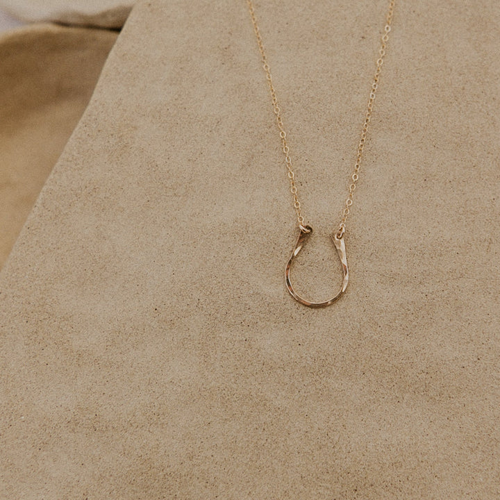 Gold necklace with a horseshoe pendant on a beige surface