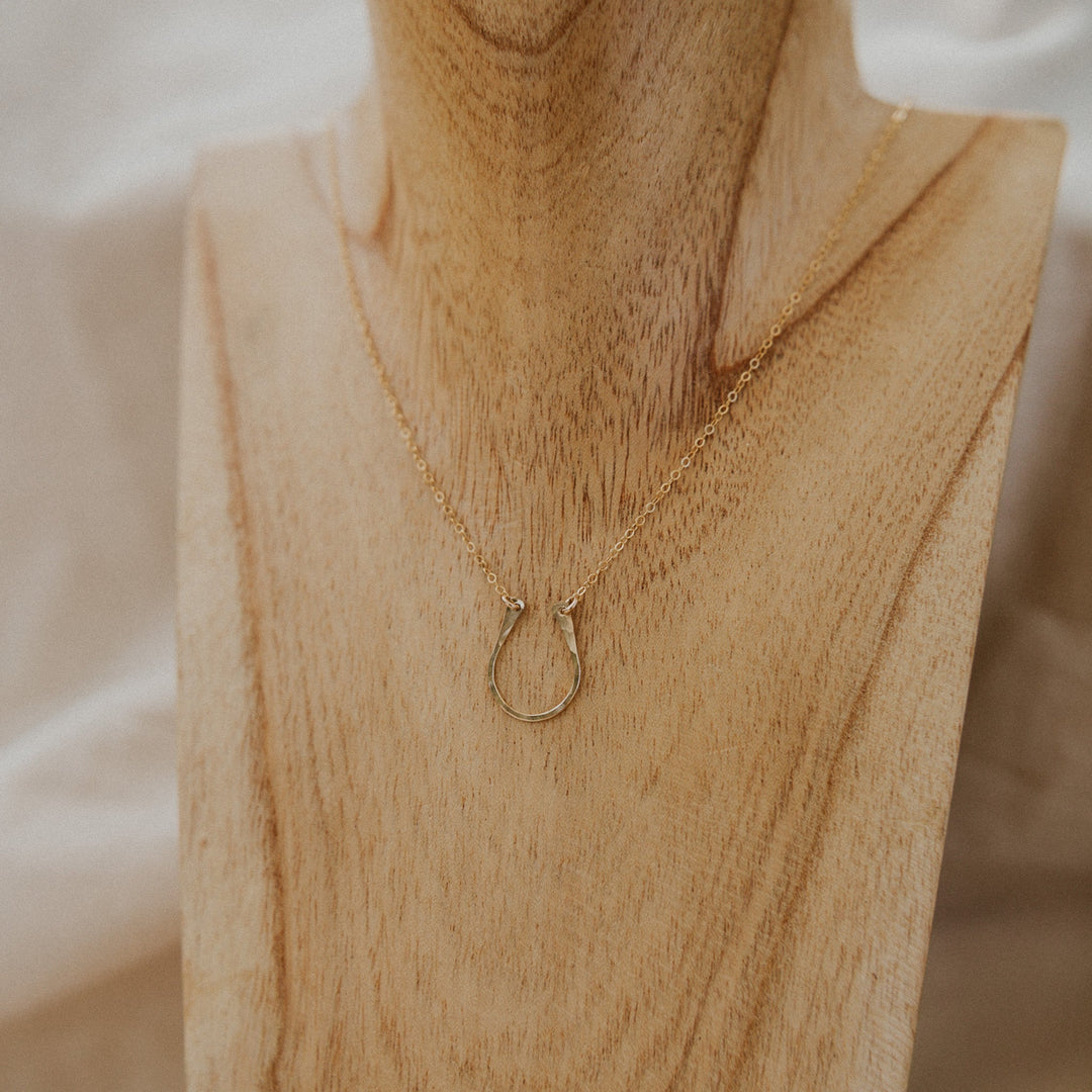 Gold necklace with a horseshoe pendant on a wooden stand.