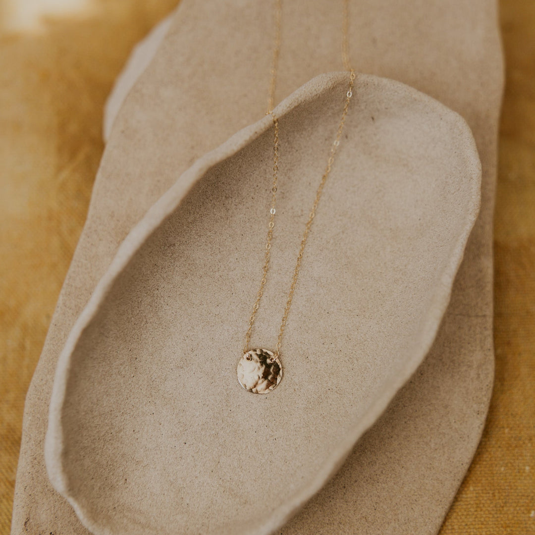 Gold necklace with a pendant on a textured beige surface
