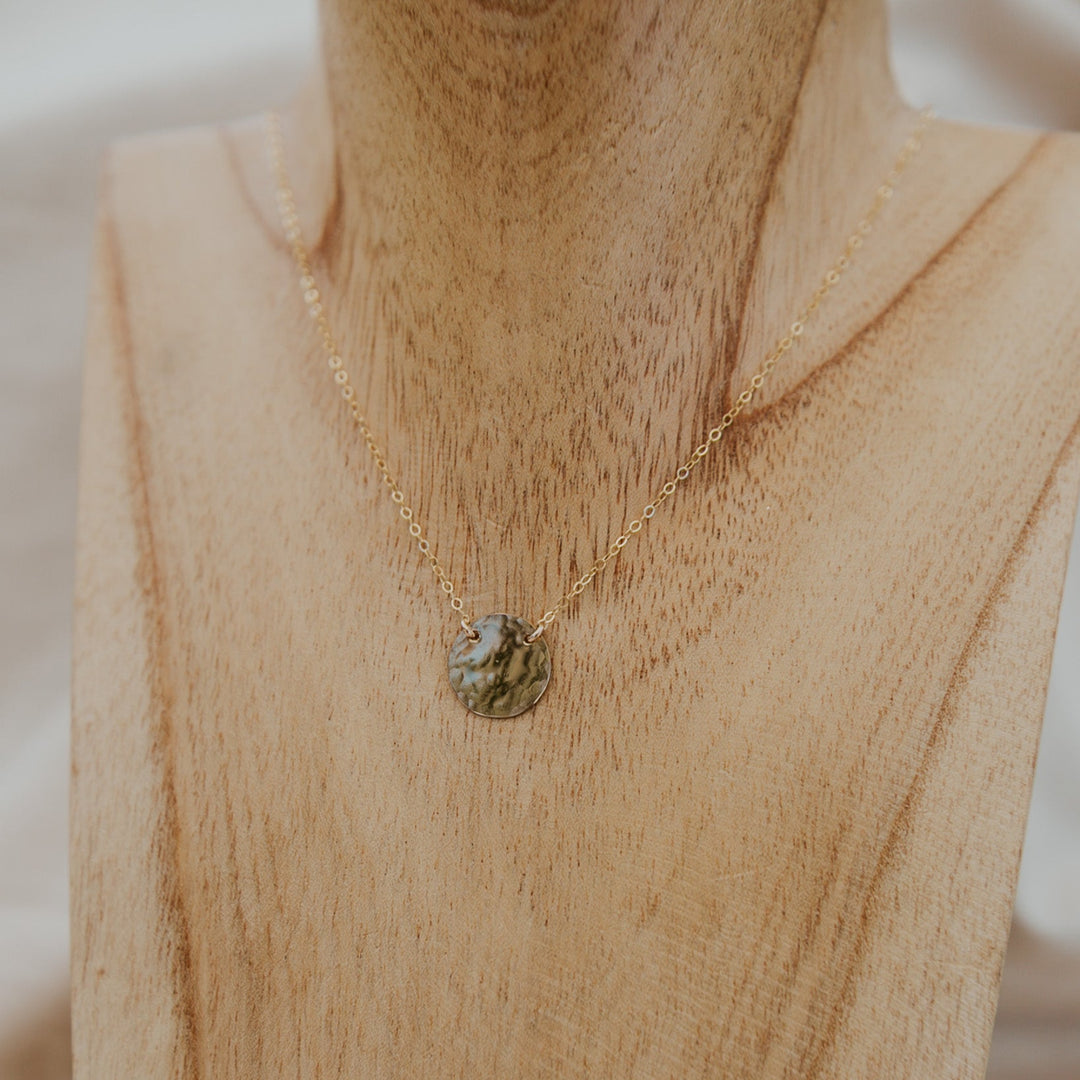 Gold necklace with a pendant on a wooden mannequin bust.