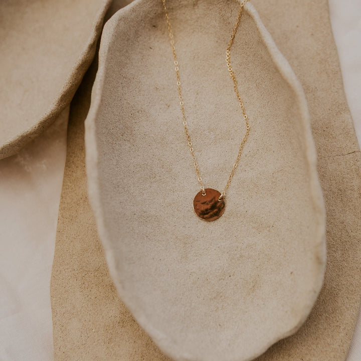 Gold necklace with a round pendant on a beige fabric background