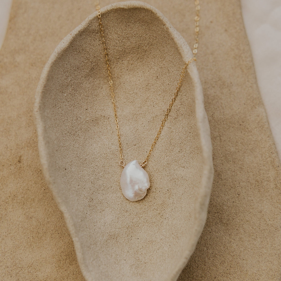 Pearl necklace on a gold chain displayed on a natural stone surface