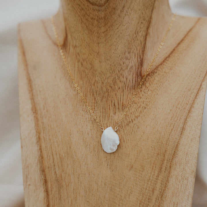 Gold necklace with a white pendant on a wooden mannequin.