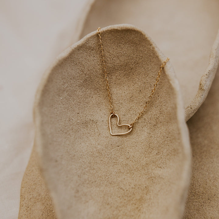 Gold heart-shaped necklace on a textured beige surface