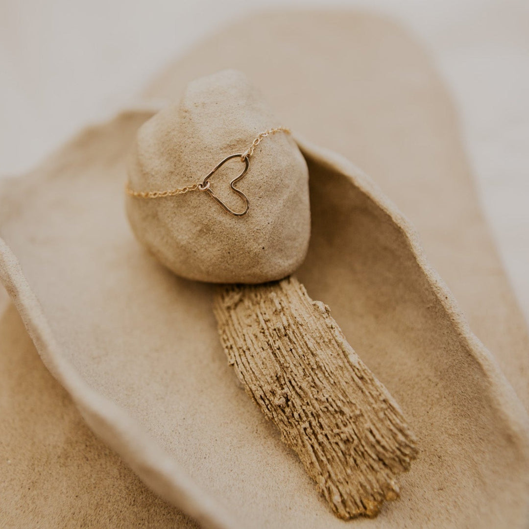 Beige heart-shaped pendant with tassel on a beige fabric background