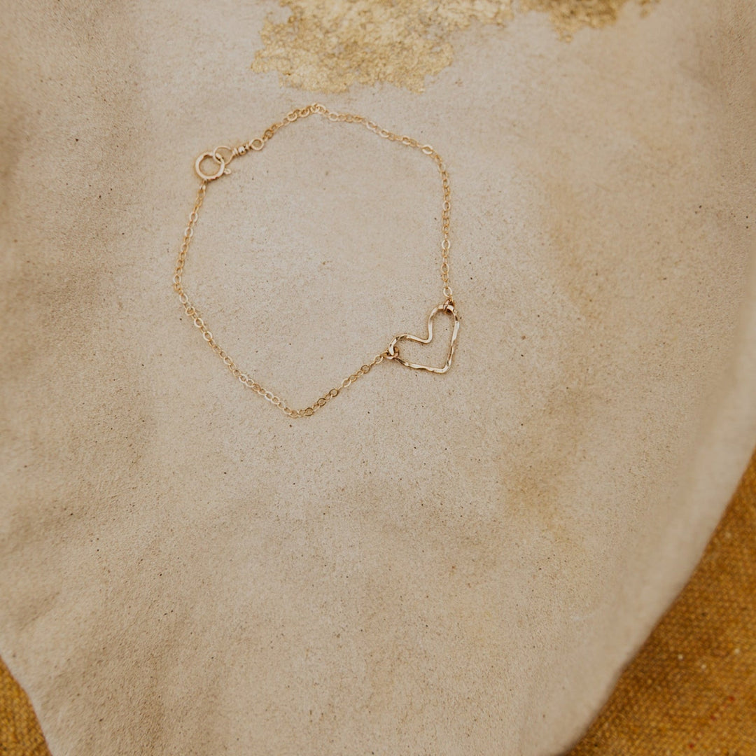 Gold bracelet with a heart-shaped clasp on a textured beige surface