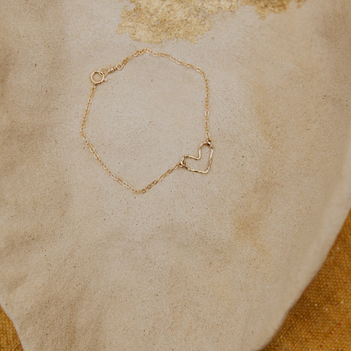 Gold bracelet with a heart-shaped clasp on a textured beige surface