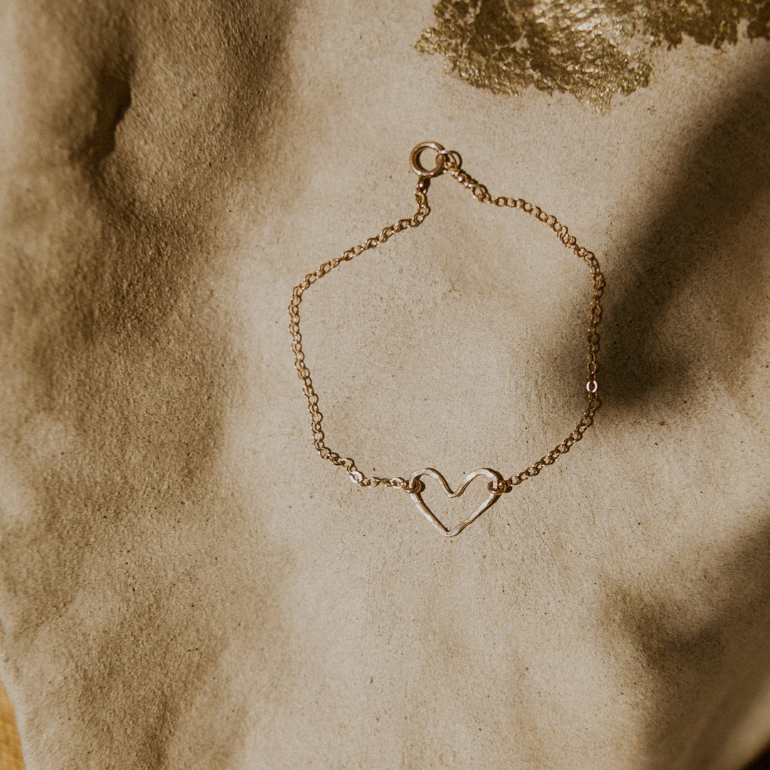 Gold bracelet with a heart charm on a textured beige surface