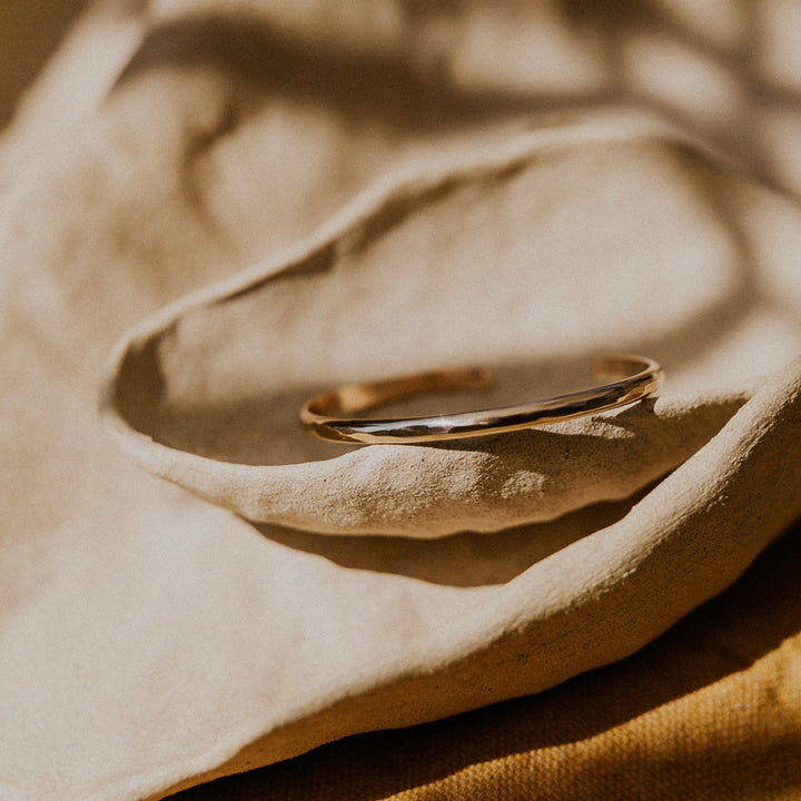 Gold hammered cuff bracelet on a textured beige surface with a warm color tone
