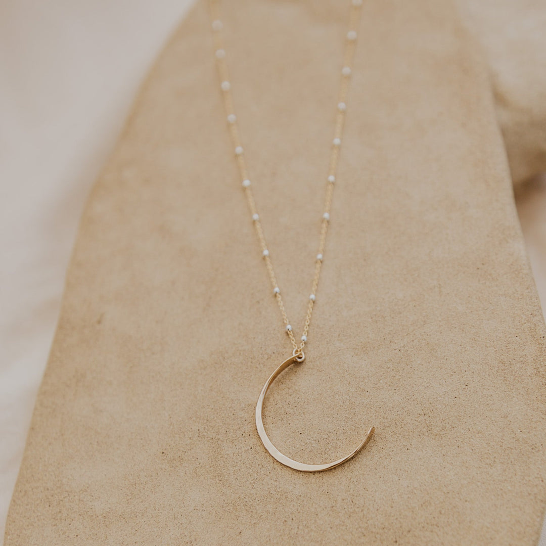 Gold crescent moon necklace on a beige surface