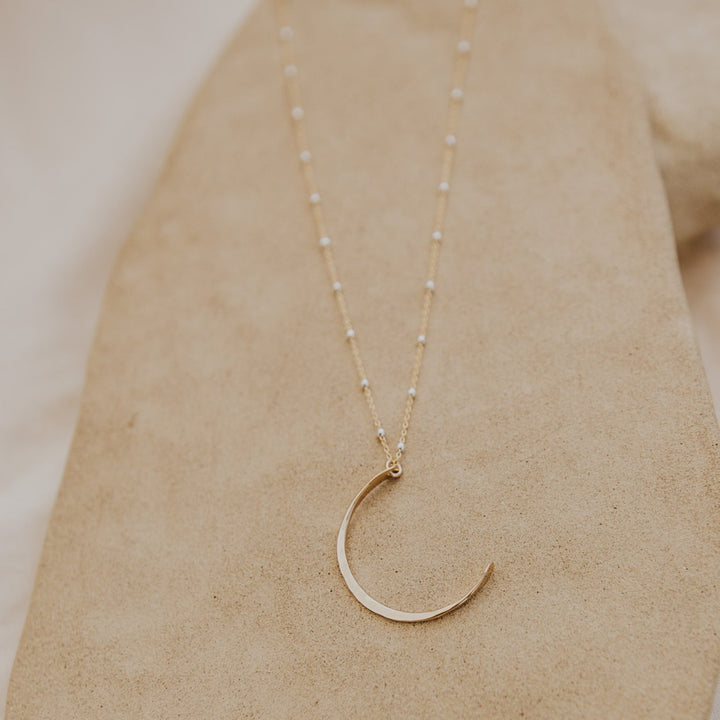 Gold crescent moon necklace on a beige surface