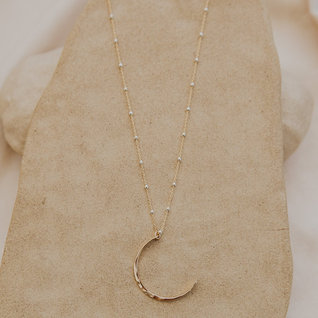Gold necklace with a crescent moon pendant on a neutral background