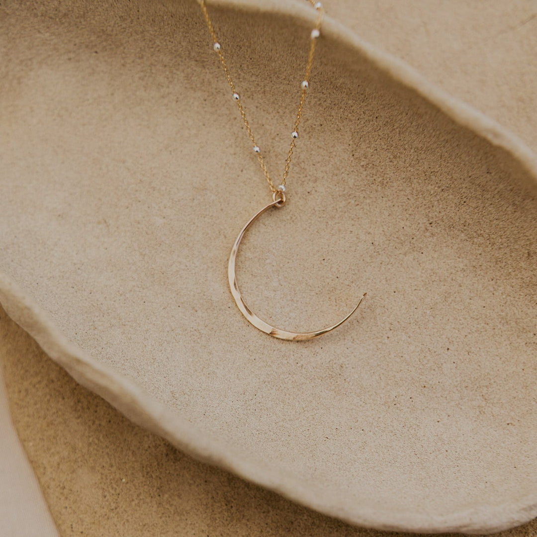 Gold necklace with a crescent moon pendant on a beige stone surface