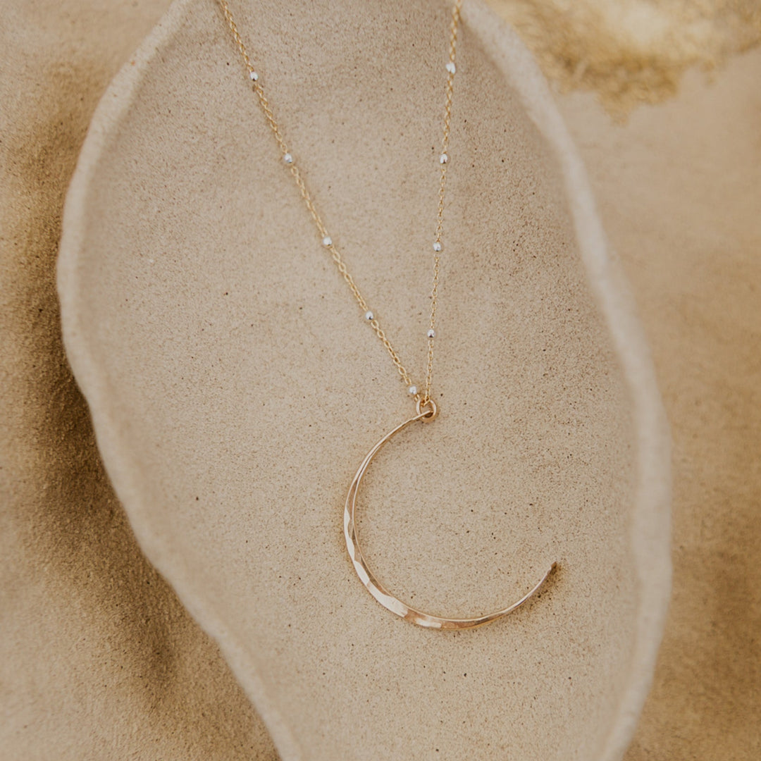 Gold necklace with a crescent moon pendant on a beige stone surface