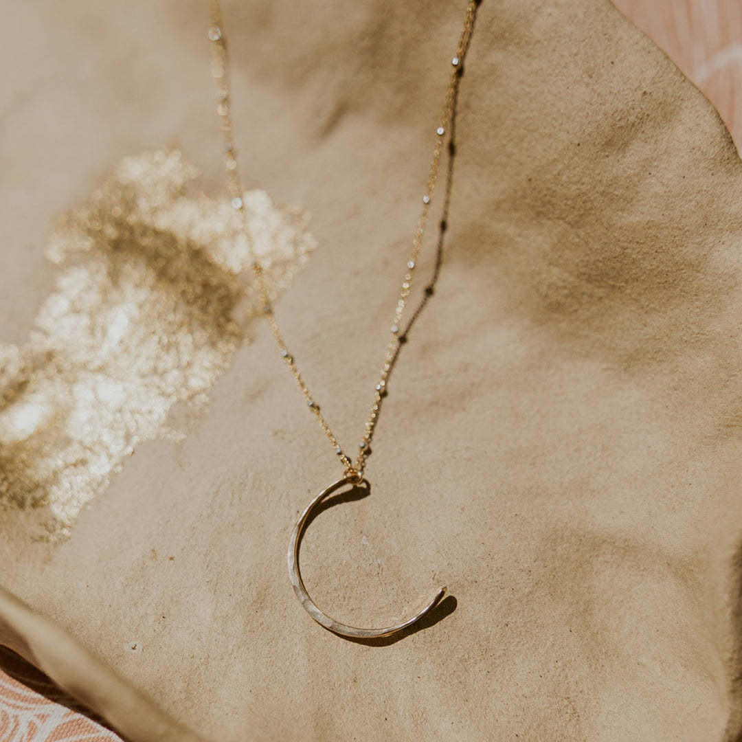 Gold necklace with a crescent moon pendant on a textured surface