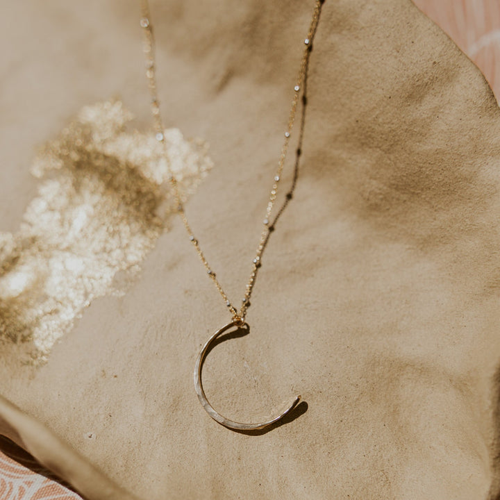 Gold necklace with a crescent moon pendant on a textured surface