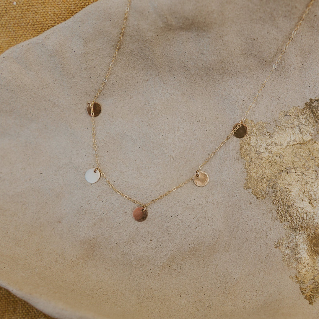 Delicate gold necklace with small circular pendants on a textured beige surface