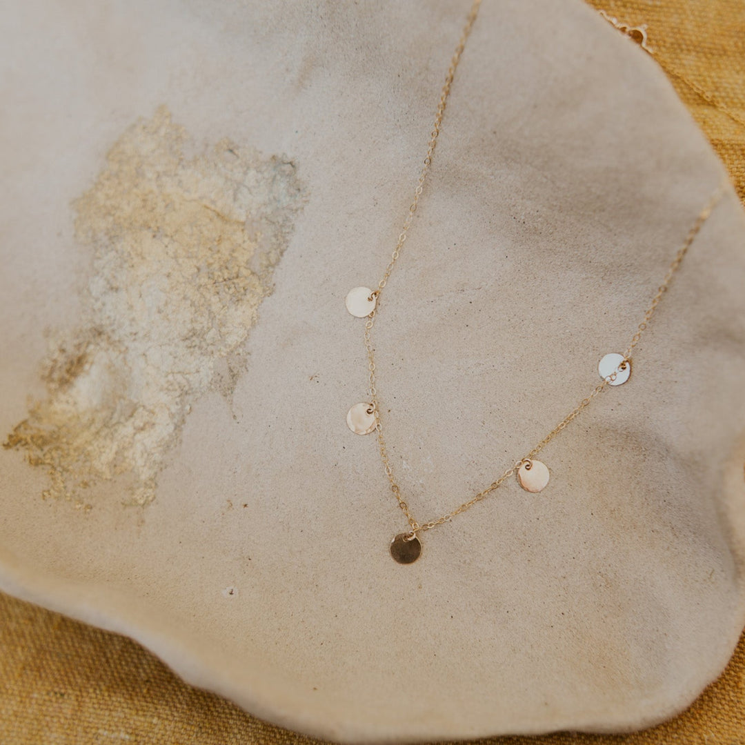 Gold necklace with small round pendants on a textured beige surface