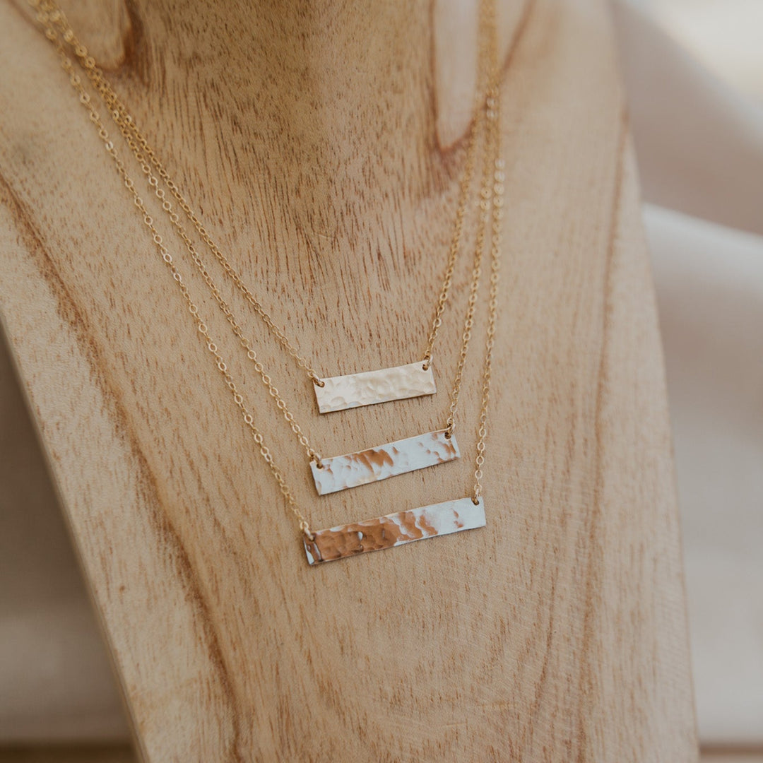 Gold necklaces with bar pendants on a wooden stand