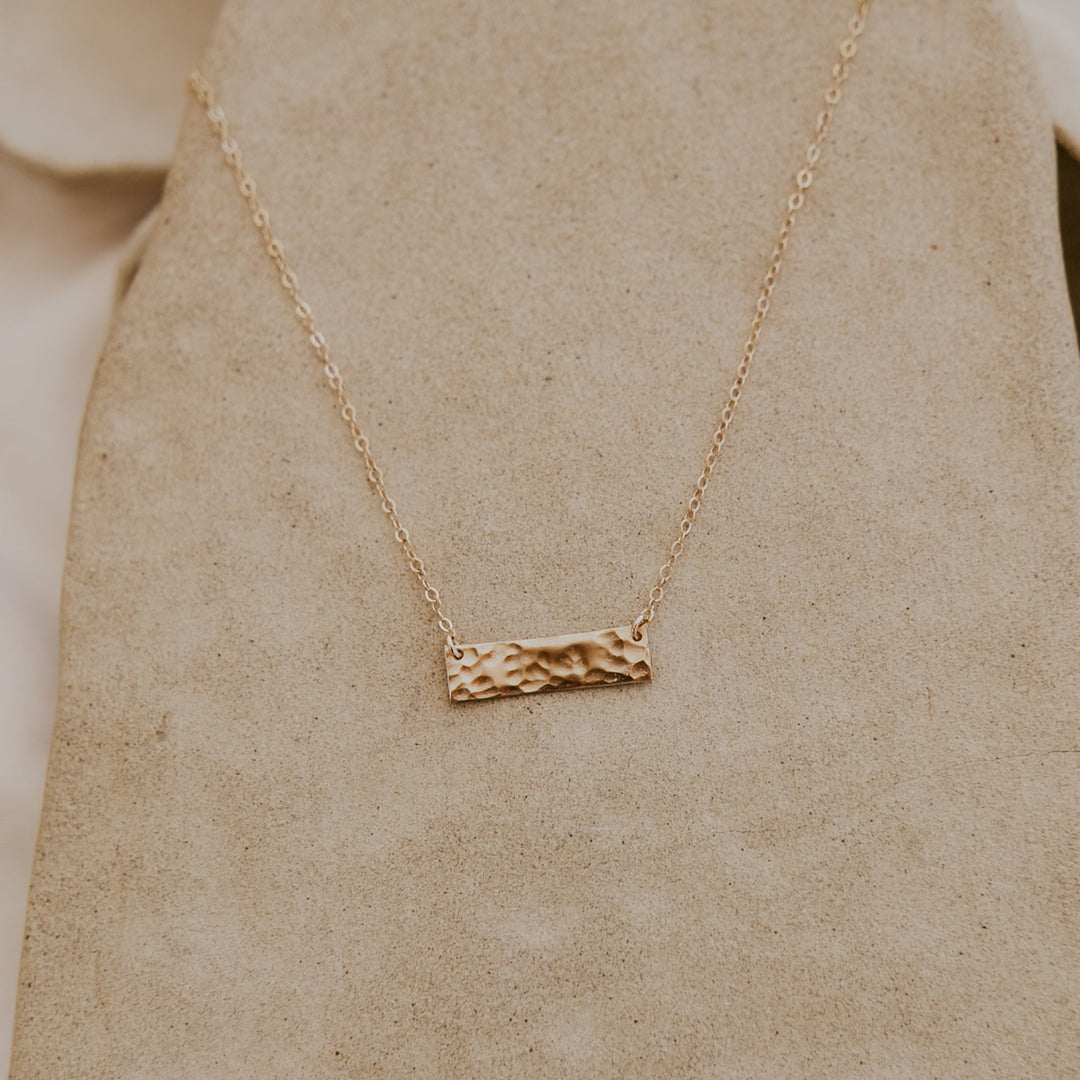 Gold necklace with a textured bar pendant on a beige background