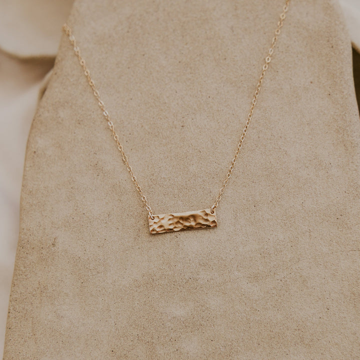 Gold necklace with a textured bar pendant on a beige background