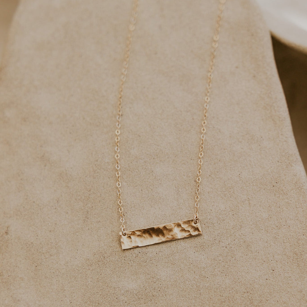 Gold necklace with a bar pendant on a beige fabric background