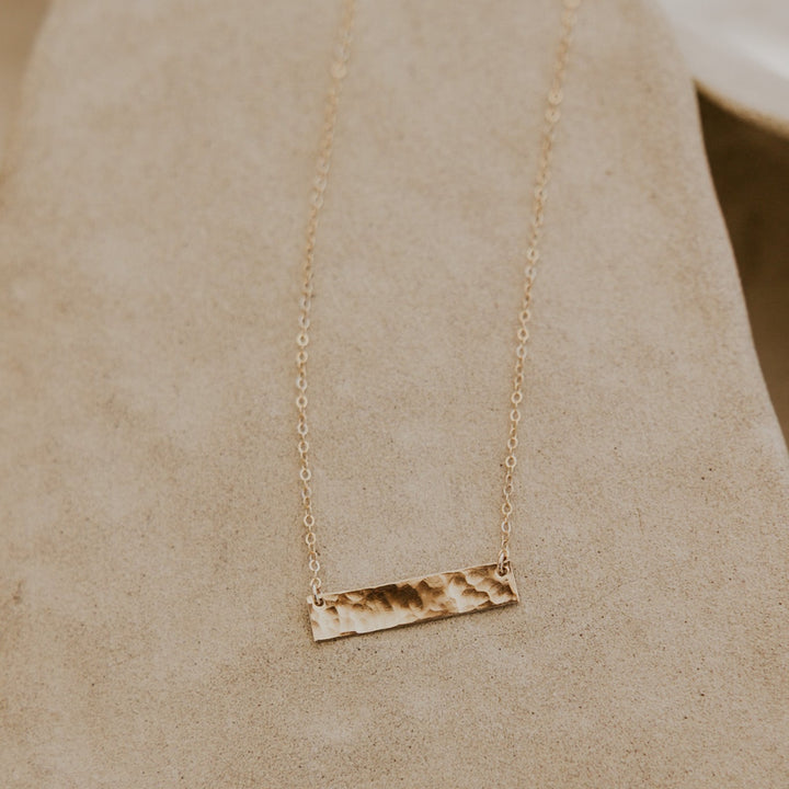 Gold necklace with a bar pendant on a beige fabric background