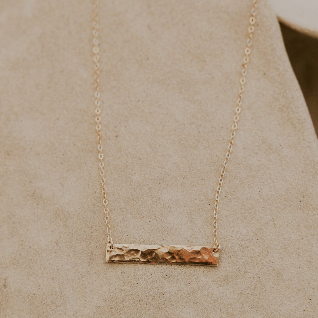Gold necklace with a bar pendant on a beige background