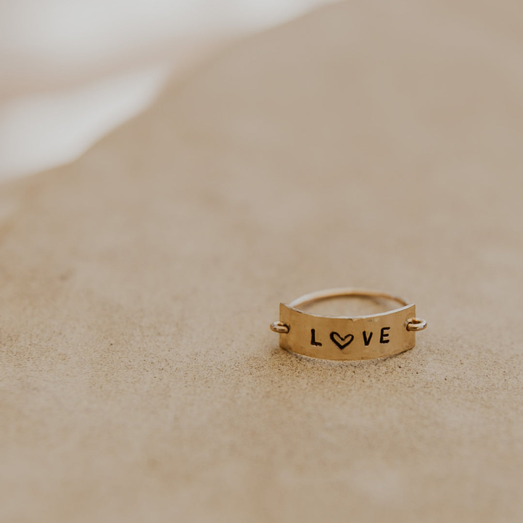 Gold ring with 'LOVE' engraving on a sandy surface
